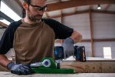 Een persoon met veiligheidsuitrusting gebruikt een snoerloze slagmoersleutel op een groen metalen armatuur.