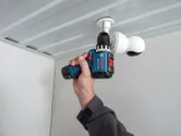 Iemand gebruikt een accuboormachine om een ​​beveiligingscamera aan het plafond te bevestigen.