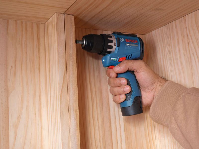 Iemand die een accuboormachine gebruikt om een ​​houten kast in elkaar te zetten.