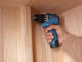 Iemand die een accuboormachine gebruikt om een ​​houten kast in elkaar te zetten.