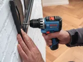 Iemand gebruikt een accuboormachine om een ​​beugel op een witte bakstenen muur te bevestigen.