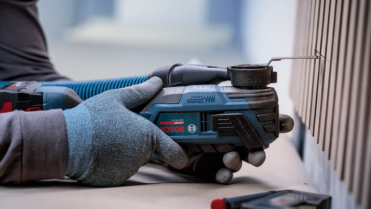 Een persoon die veiligheidsuitrusting draagt, gebruikt een elektrisch gereedschap om een ​​groef in een houten paneel te zagen.