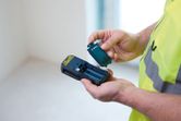 Een persoon die veiligheidsuitrusting draagt, plaatst een batterij in een draagbaar meetinstrument.
