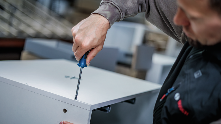 Een persoon die meubels in elkaar zet met een handmatige schroevendraaier.