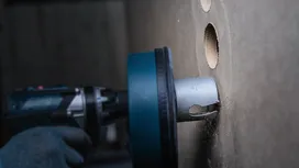 Een persoon die veiligheidsuitrusting draagt, gebruikt een boormachine met een gatenzaag om een ​​gat in een muur te zagen.