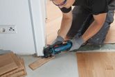 Een persoon die veiligheidsuitrusting draagt, snijdt een vloerplank bij met een multitool.
