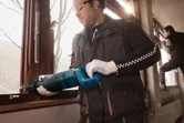 Een persoon die veiligheidsmateriaal draagt, gebruikt een reciprozaag om een raamkozijn door te zagen.