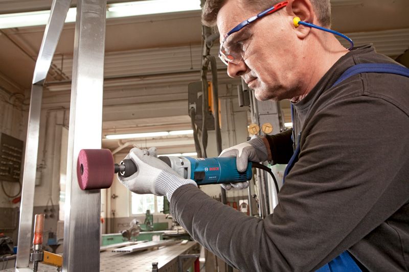 Een persoon die veiligheidsuitrusting draagt, gebruikt een rechte slijper om een metalen oppervlak te polijsten.