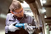 Een persoon die veiligheidsuitrusting draagt, slijpt het binnenoppervlak van een grote metalen ring met een rechte slijper.