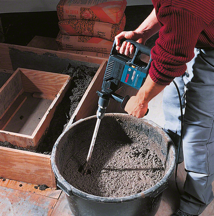 Een arbeider mengt cement in een emmer met behulp van een boormachine.