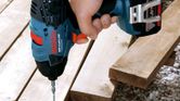 Човек използва безжичен ударен винтоверт, за да завие винт в дървени дъски.