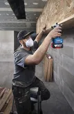 Човек, носещ предпазни средства, използва рутер на дървен рафт.