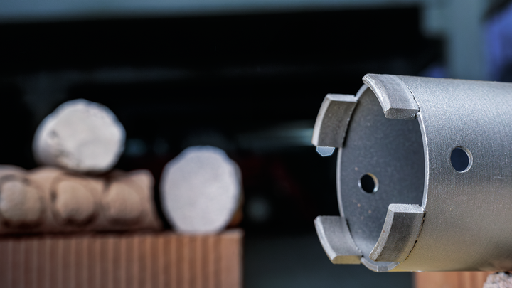 Едър план на метално свредло, използвано за пробиване в подредени бетонни цилиндри.