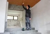 Човек измерва таван с рулетка, воден от лазерен нивелир.