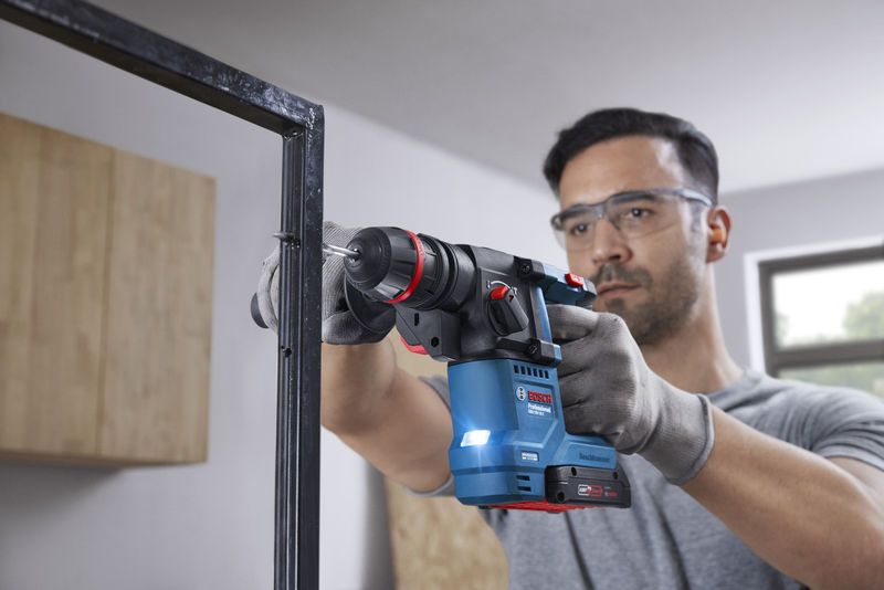 Човек, носещ предпазни средства, пробива метална рамка с помощта на безжичен перфоратор.