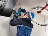 Una persona que usa equipo de seguridad perfora un techo de hormigón con un martillo perforador inalámbrico.