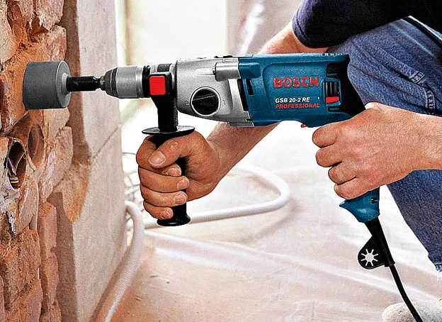 Una persona perfora un agujero circular en una pared de ladrillos utilizando un taladro de impacto.