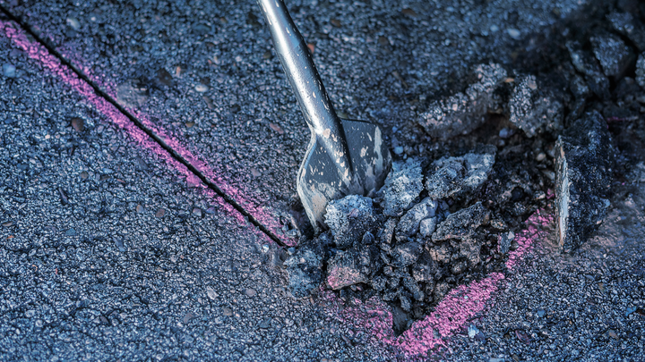 Broca de cincel rompiendo el asfalto a lo largo de una línea guía de color rosa.