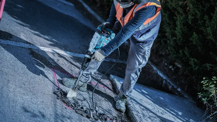 Una persona que usa equipo de seguridad rompe el pavimento con una herramienta de demolición eléctrica.