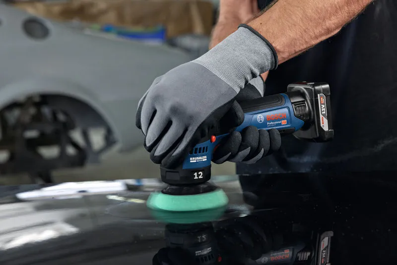 Una persona que usa equipo de seguridad pule la superficie de un automóvil con una pulidora inalámbrica.