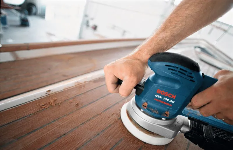 Una persona utiliza una lijadora orbital aleatoria para alisar la madera en la cubierta de un barco.