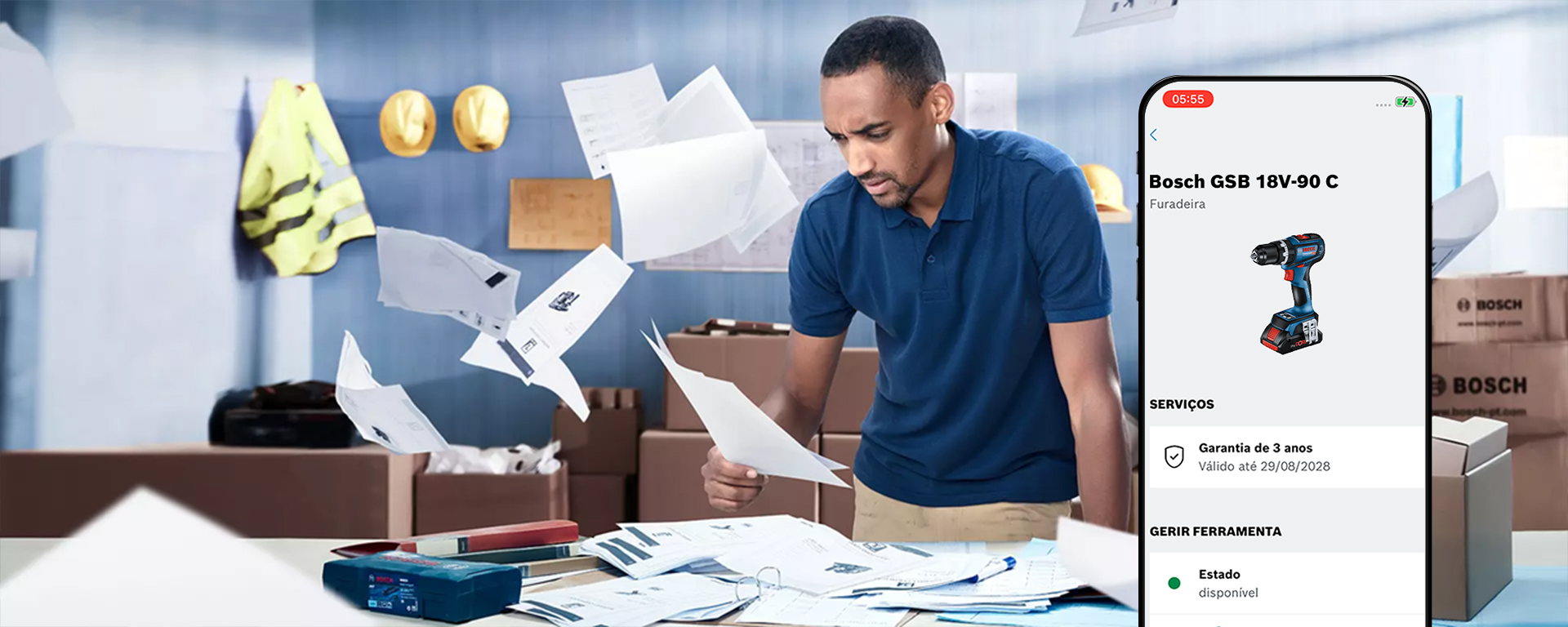 Um homem com uma camisa azul revisa documentos em uma mesa cheia de papéis, uma furadeira Bosch e caixas.