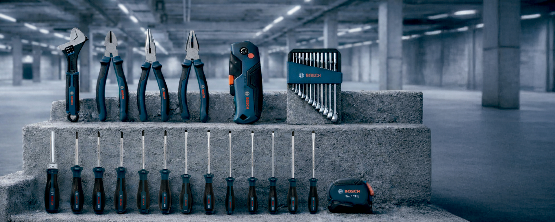 Uma exibição de ferramentas profissionais Bosch dispostas em degraus de concreto, incluindo alicates, chaves de fenda e um conjunto de pontas.