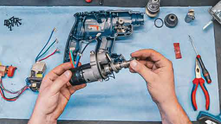 Furadeira Bosch Professional desmontada, mãos segurando uma parte do motor, ferramentas próximas.