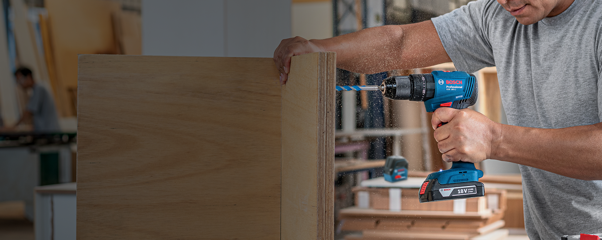 Uma furadeira Bosch Professional é utilizada em um painel de madeira em uma oficina.