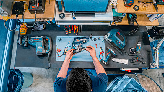 Uma pessoa conserta ferramentas Bosch em uma bancada de trabalho com várias ferramentas e peças.