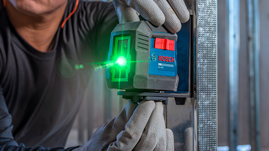 Uma pessoa com luvas fixa um nível a laser Bosch Professional a uma estrutura de metal, com um feixe de laser verde visível.