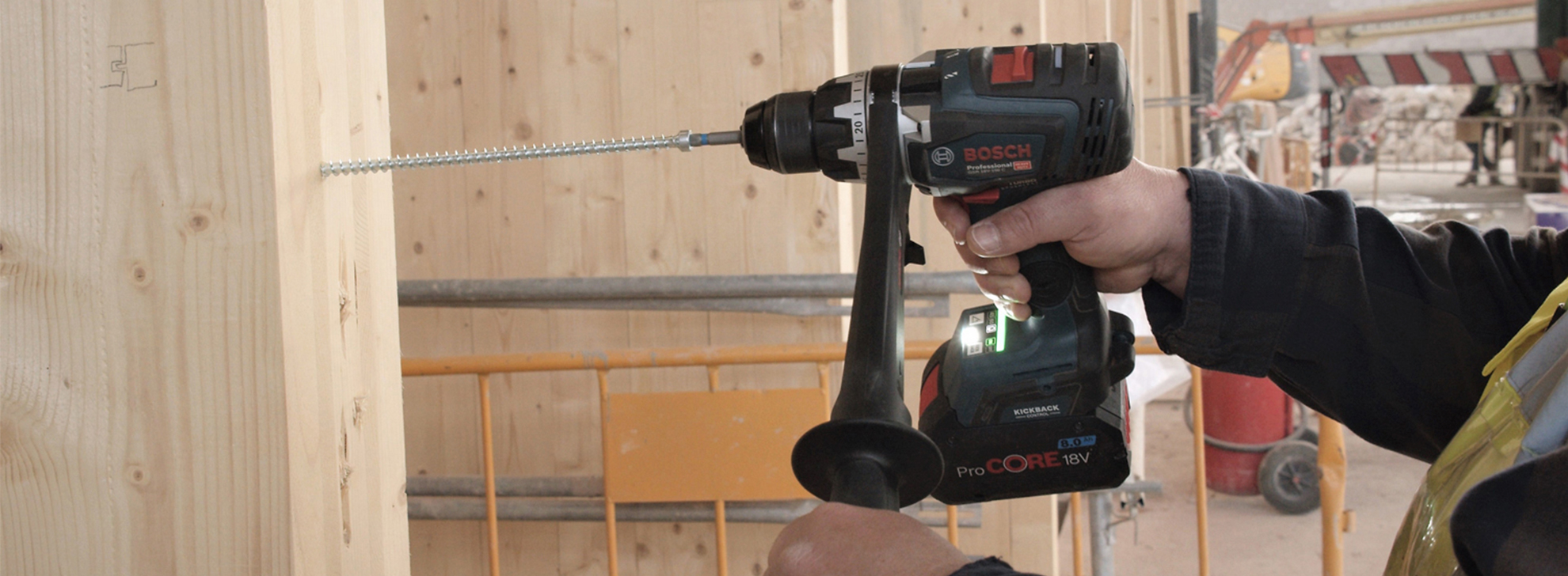 Uma furadeira Bosch Professional está sendo usada em vigas de madeira em um canteiro de obras.