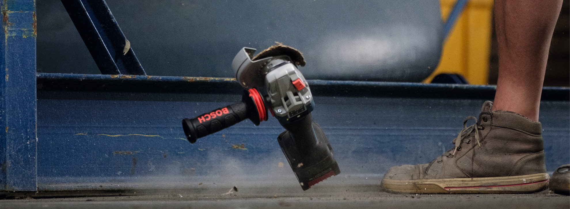 Uma ferramenta Bosch Professional paira acima de um chão empoeirado, ao lado de um pé.