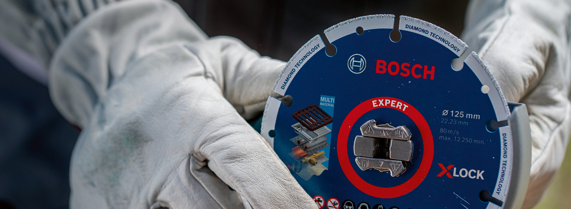 Uma lâmina de diamante Bosch Expert X-LOCK segurada por mãos com luvas ao ar livre.