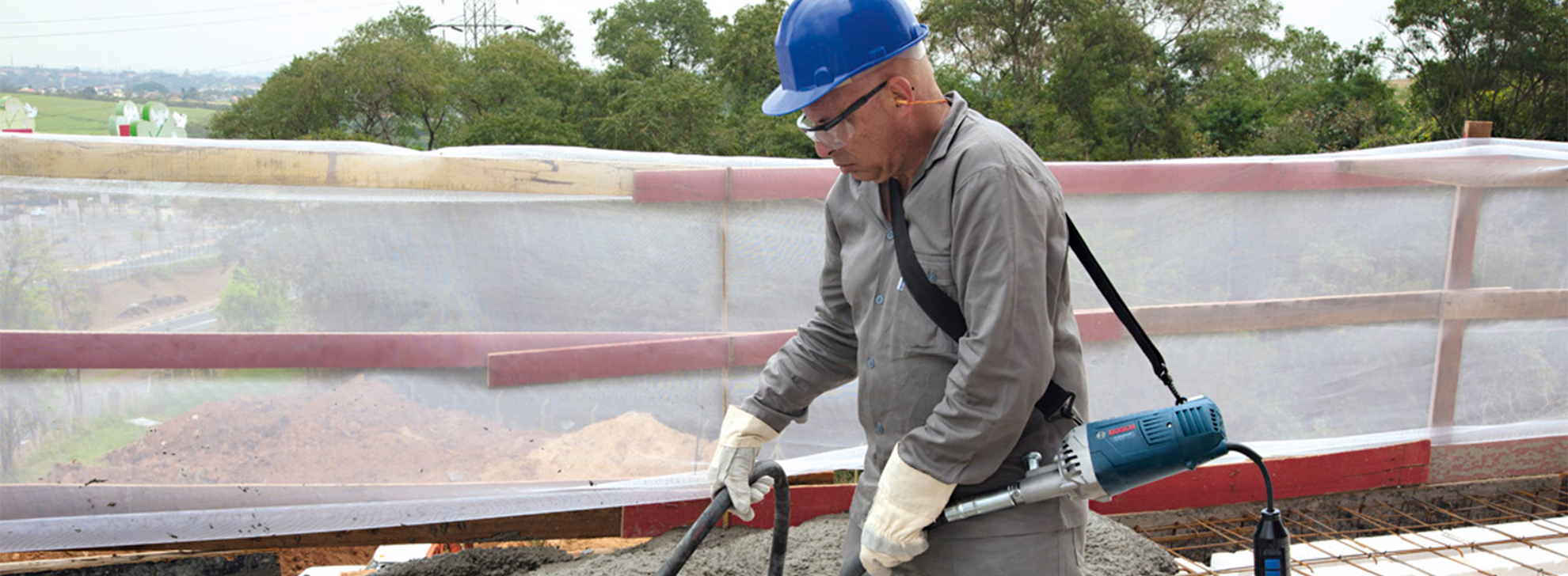 Um trabalhador com um capacete azul utiliza um vibrador de concreto Bosch Professional ao ar livre.