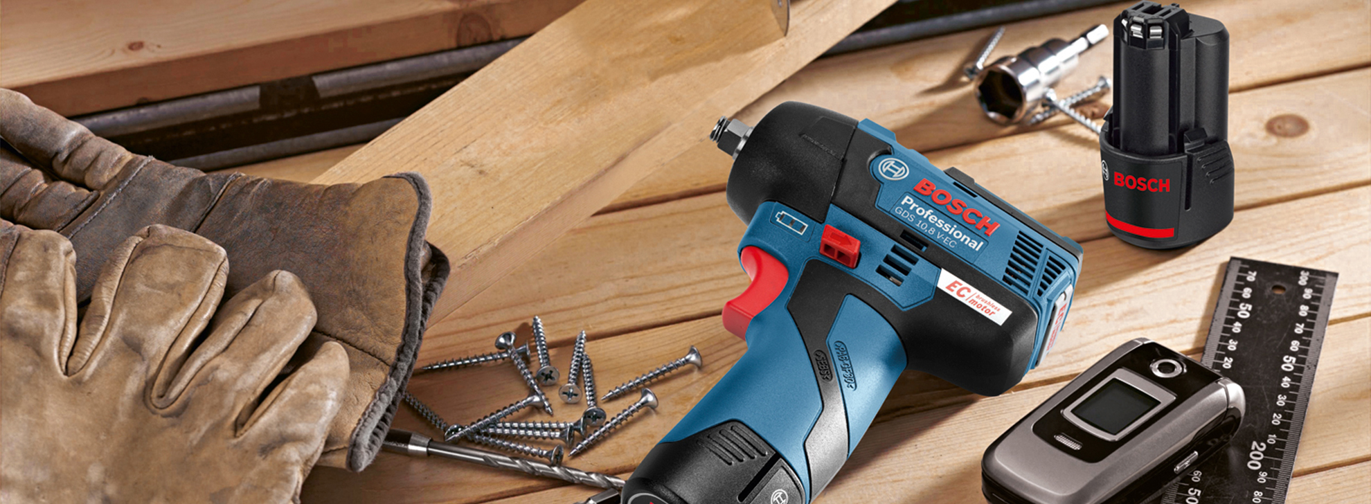 Uma furadeira Bosch Professional repousa sobre tábuas de madeira com luvas e parafusos.