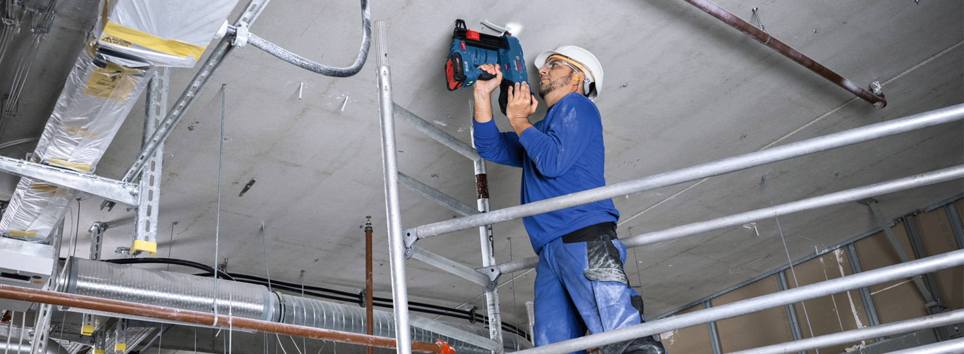 Um trabalhador usando uma ferramenta Bosch Professional em um andaime, focado no teto.