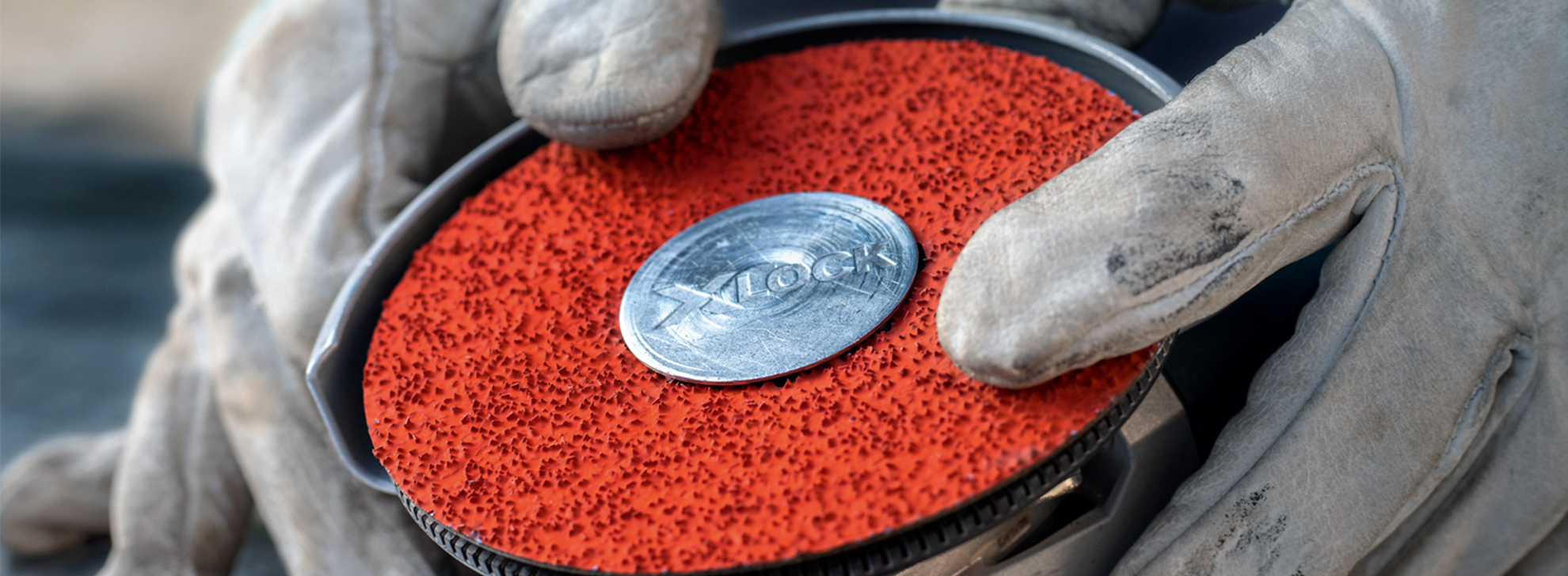 Uma pessoa com luvas segura um disco de lixa vermelho com um centro de metal.