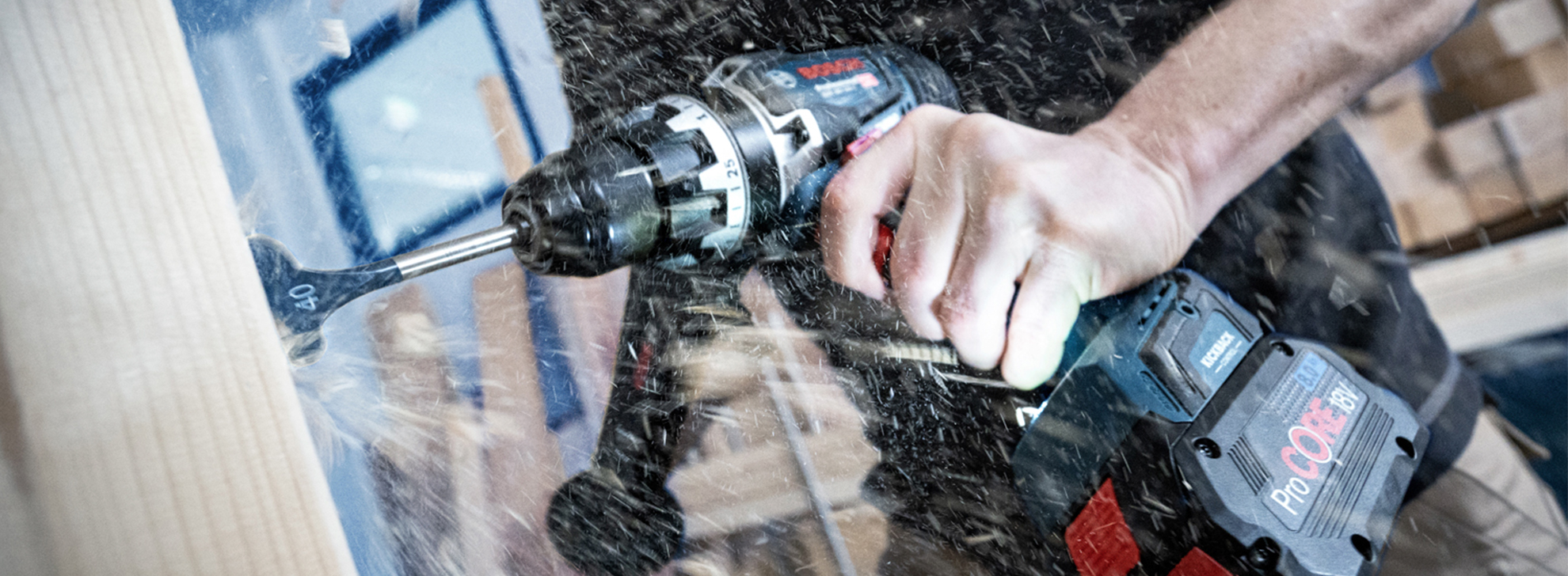 Uma furadeira Bosch Professional é utilizada em uma superfície de madeira, criando serragem.