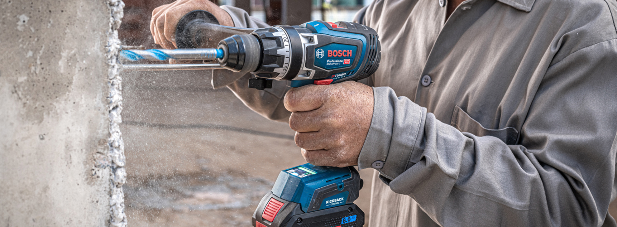 Uma furadeira Bosch Professional em uso, perfurando uma parede de concreto ao ar livre.