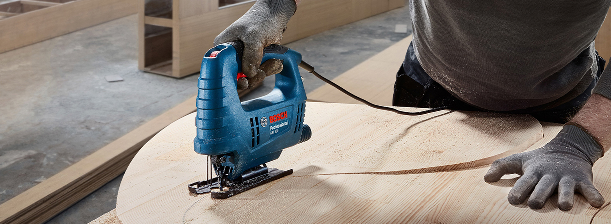 Uma serra tico-tico azul da Bosch Professional corta um círculo de madeira em uma bancada.
