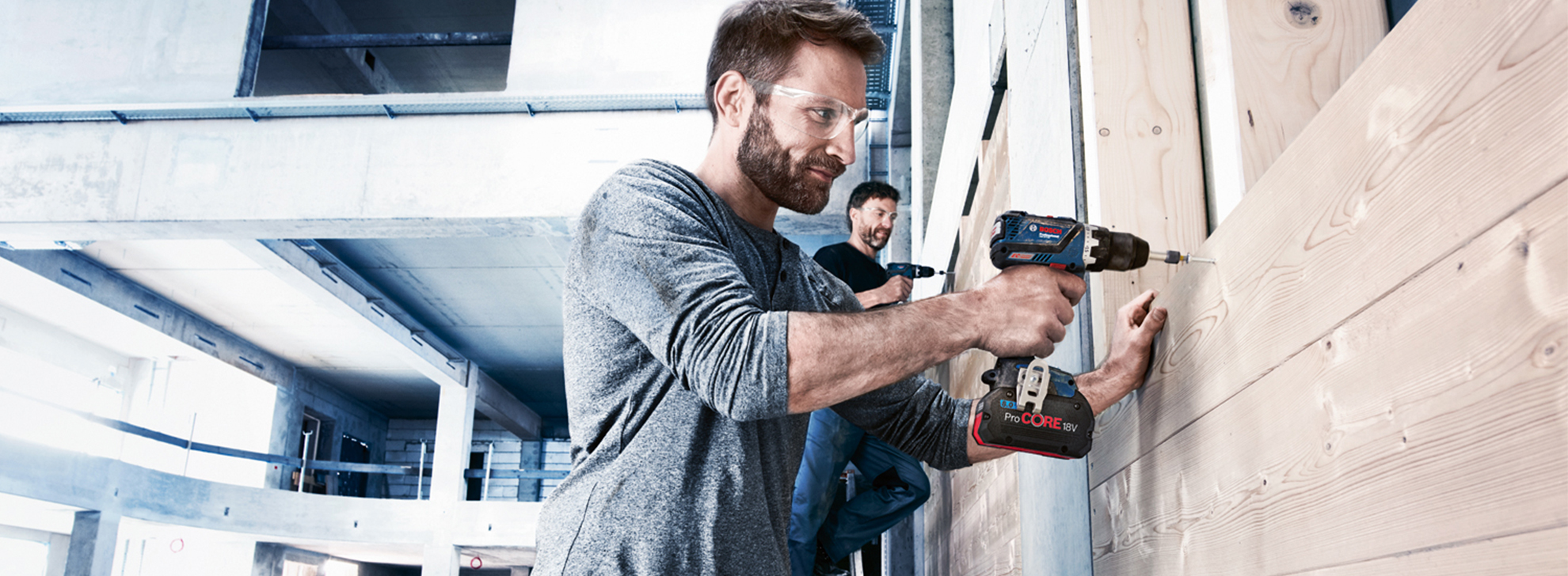 Um homem perfura painéis de madeira em um canteiro de obras moderno.