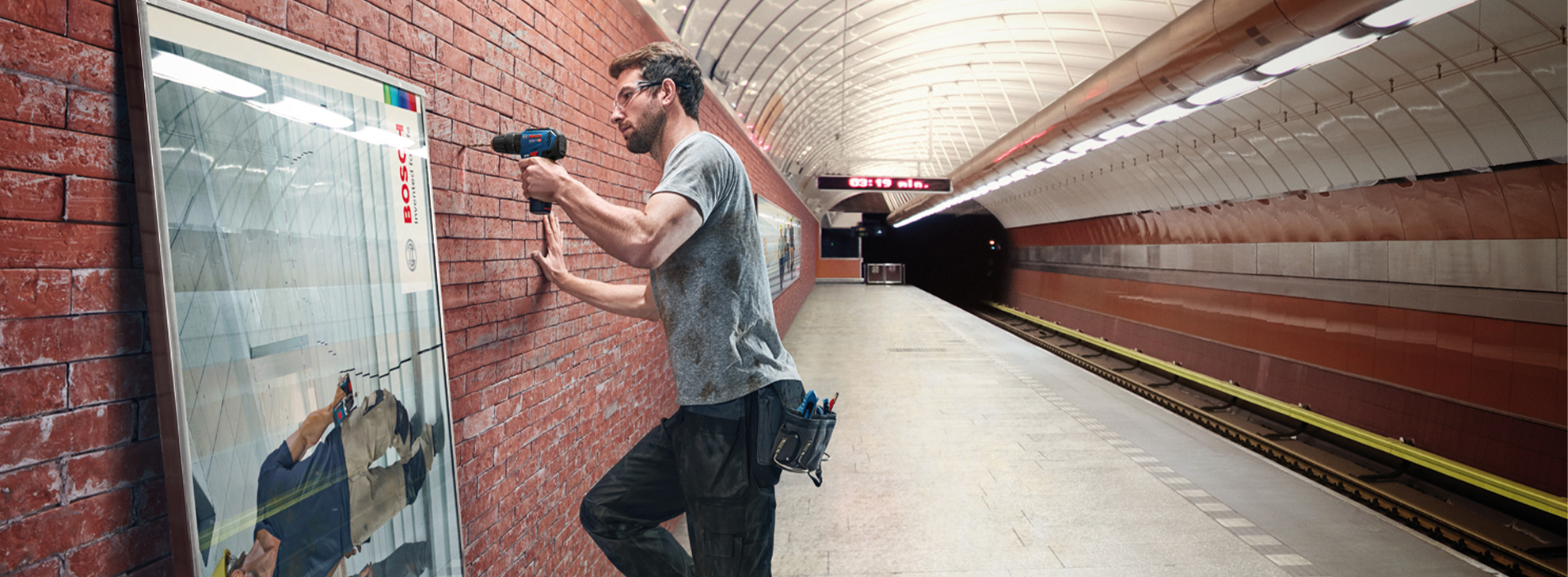 Um homem perfura uma parede de tijolos em uma estação de metrô.