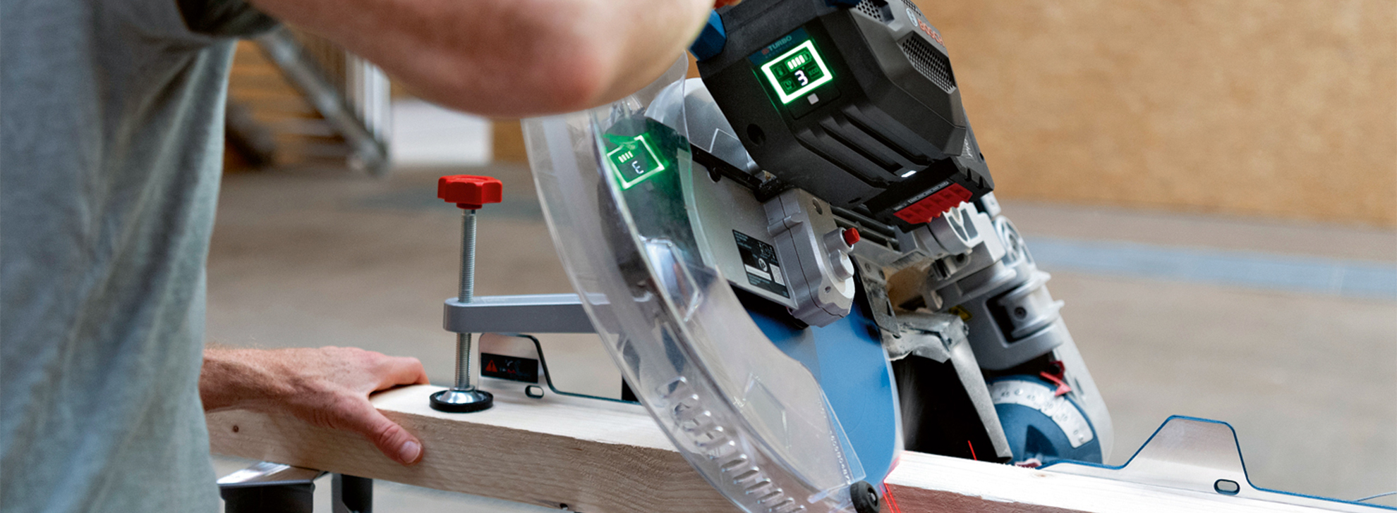 Uma serra circular profissional Bosch corta uma viga de madeira, com uma mão guiando-a.