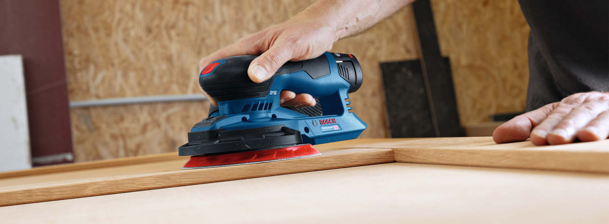 Uma lixadeira azul Bosch Professional paira sobre uma superfície de madeira.