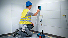 Um trabalhador com um capacete azul usa uma ferramenta Bosch em uma parede de azulejos.