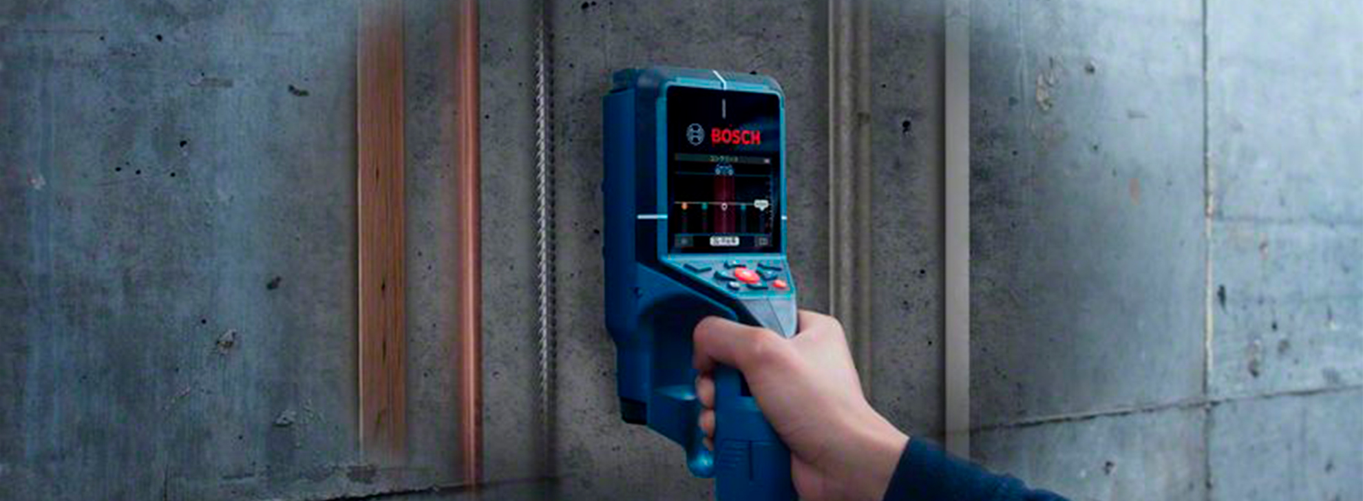 Um scanner de parede Bosch Professional azul é segurado contra uma parede de concreto.