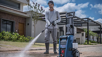 Um homem vestido com roupas cinzas usa um lavador de alta pressão Bosch Professional ao ar livre.