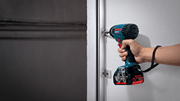 Uma furadeira azul Bosch Professional está sendo usada para parafusar em uma parede.