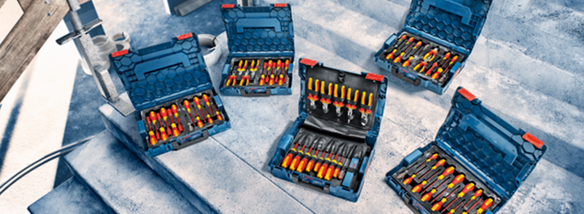 Cinco caixas de ferramentas azuis da Bosch Professional abertas com chaves de fenda amarelas e pretas em escadas de concreto.